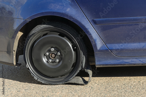 Foto Shredded tyre disintegrated from the rim of a blue car on a road