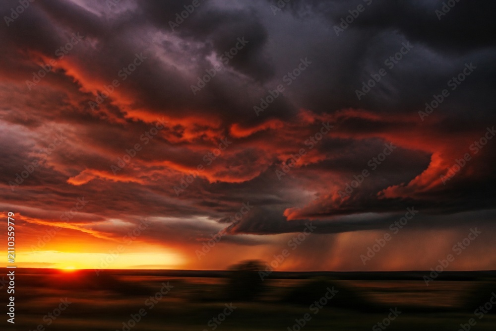 Fototapeta premium Heavy storm clouds at dusk with rust-red edges over a blurred landscape.