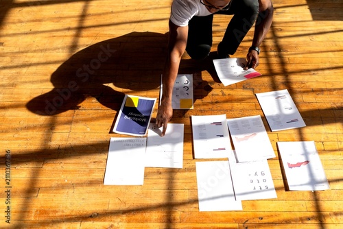 Photography Person organizing documents on a wooden floor in bright sunlight.
