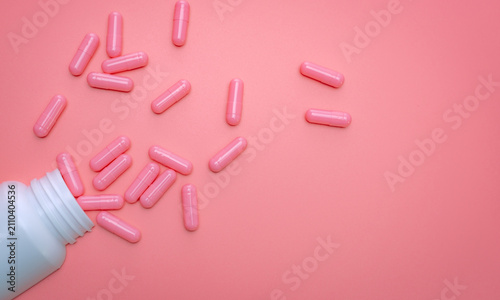 Foto Pink capsule spread out of white plastic drug bottle