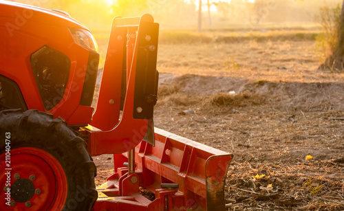 Bild auf Leinwand Orange tractor parked at rice farm in summer morning with sunlight