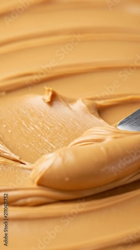 A smooth metal knife spreading creamy peanut butter on a flat surface