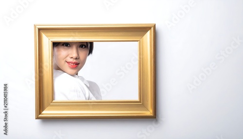 A woman's face, framed by a gilded rectangular border, peeks partially from behind it, on a bright white background