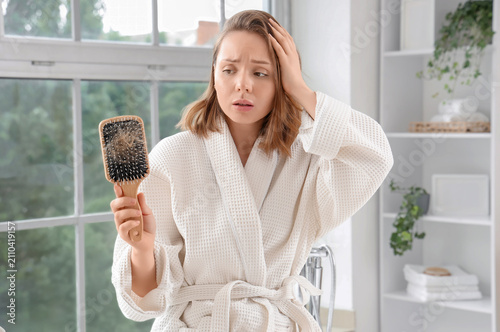 Quadro su tela Concerned young woman in a bathrobe holding a hairbrush full of fallen hair, hai