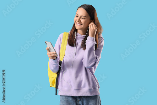 Smiling young woman student with backpack and wired earphones listening to mu...