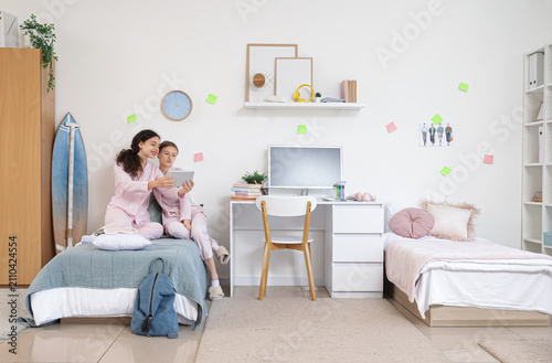 Female students with tablet computer taking selfie in dorm room