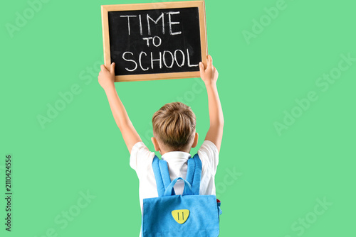 Little boy holding chalkboard with text TIME TO SCHOOL on green background, b...