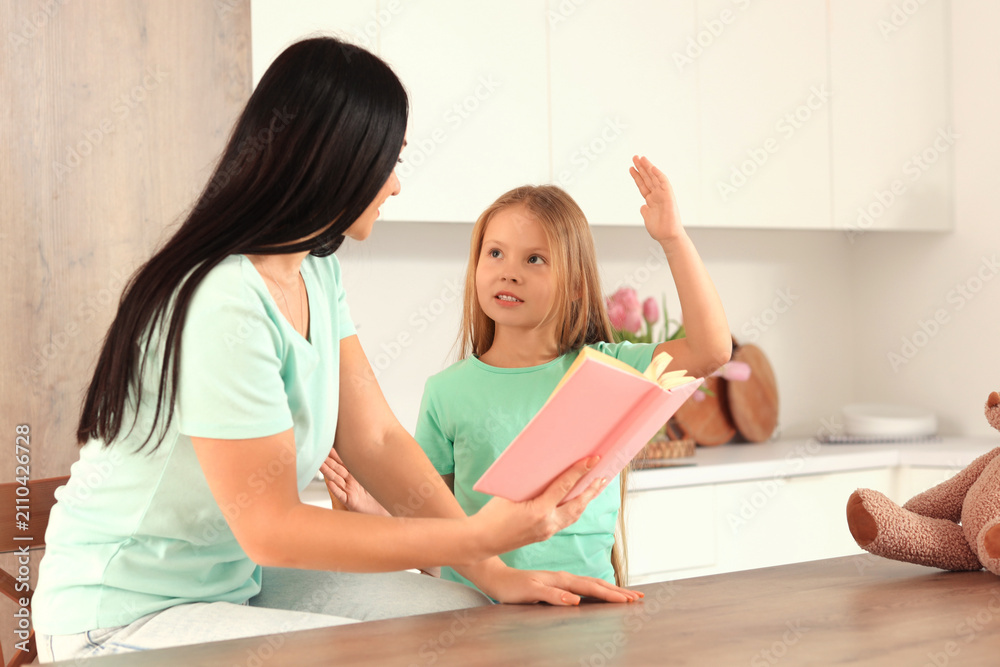 Obraz premium Happy mother with her little daughter reading book in kitchen