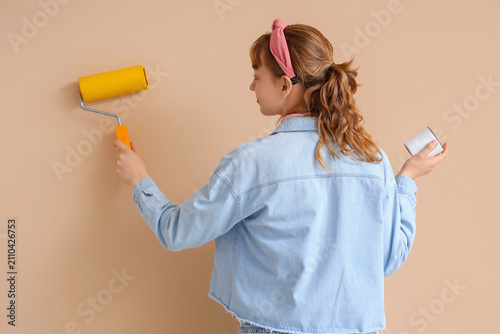 Canvas-taulu Young woman with paint roller and can on beige background, back view