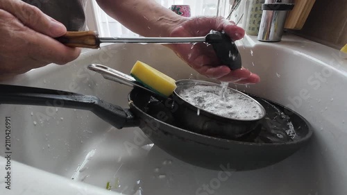 A person washing a cooking pot and pan in the kitchen sink.