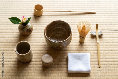 Tapety artystyczne 畳の上に丁寧に配置された茶碗、茶筅、茶杓、柄杓、茶入、布巾、そして一輪の花。和室に広がる静けさと自然光が、茶の湯の美しさと心を整える時間を伝える一枚