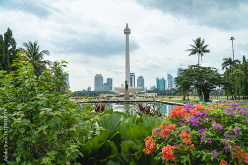 Obraz na płótnie Jakarta, Indonesia - July 24, 2026: The National Monument (Monas) rises above landscaped gardens and colorful flowers at Merdeka Square, with Jakarta's skyline in the background