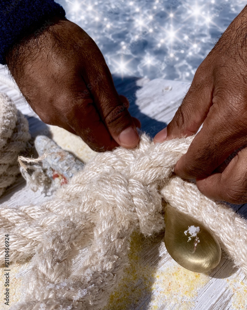 Fototapeta premium Close up of hands tying a manila rope knot on a brass cleat at a sunlit wooden pier for nautical craft and maritime style concepts
