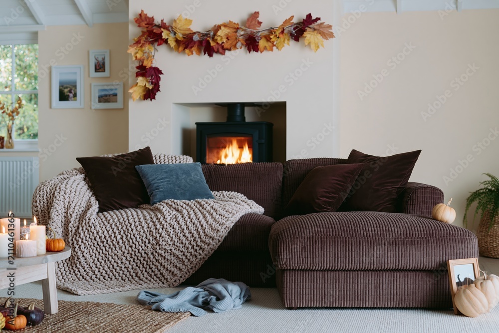 Obraz premium Cozy autumn living room featuring a brown sectional sofa with knit throws and a glowing fireplace for seasonal home decor and interior design