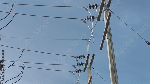 Pan up video of bare aluminum cables preparing for connection on high voltage concrete poles, industrial electrical power grid infrastructure construction under a blue sky.