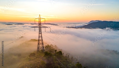 Aerial shot shows an electricity pylon, shrouded in mist, with a sunrise over rolling hills and mountains in the background