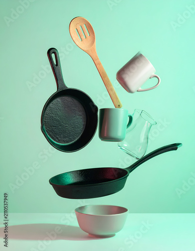 Levitating kitchen utensils cast iron pans wooden spoon and ceramic mugs against a turquoise background