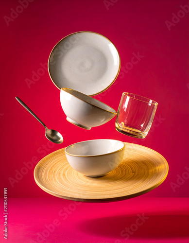 Levitation of ceramic plates and bowls with spoon and glass against a vibrant pink background