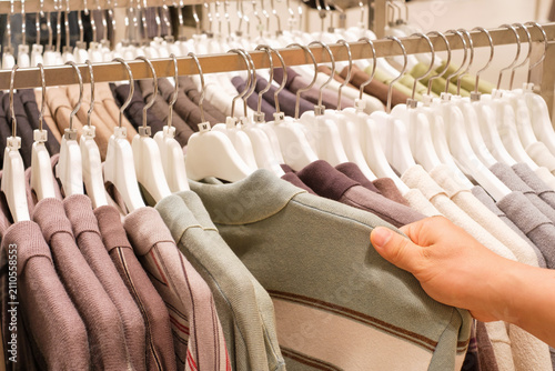 Man chooses clothes hanging on hanger in store.