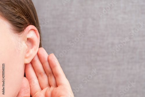 The woman listens attentively with her palm to her ear close-up on gray background, news concept.