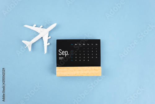 September 2027 black wooden calendar and airplane toy on blue color background.