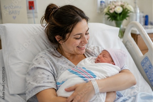 Mother holding newborn baby in hospital recovery room postpartum