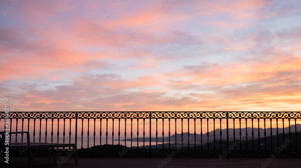 Obraz premium Wrought iron railing silhouetted against a pink and orange coastal sunset