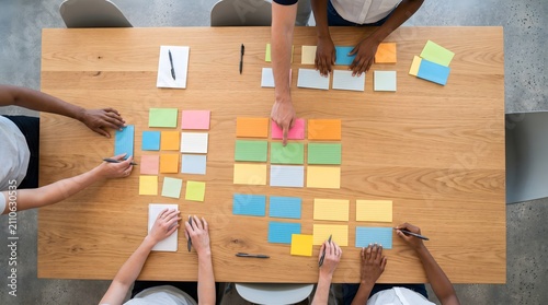 Overhead view of diverse hands arranging colorful sticky notes on a wooden table, symbolizing brainstorming, project planning, and creative problem-solving in a collaborative