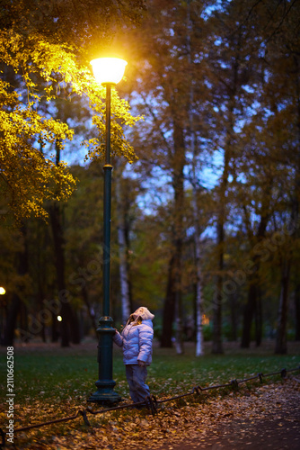 Child playing near a streetlamp in an autumn park during twilight hours