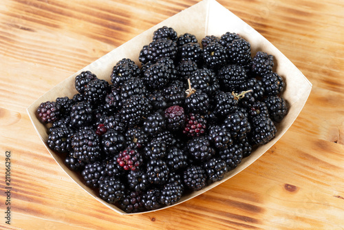 Fresh ripe blackberries in an eco-friendly paper tray on a rustic wooden table