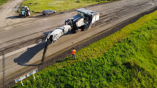 Bild auf Leinwand shot captured by drone showing a large road cold recycler machine milling asphalt and discharging reclaimed material along the side of a rural highway
