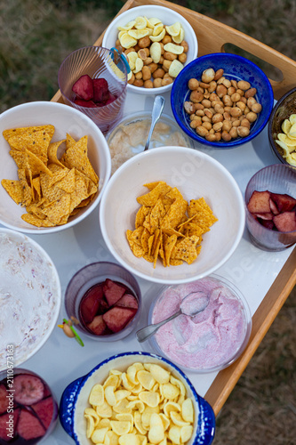 Bild auf Leinwand A wooden tray features an assortment of party snacks in bowls, including tortilla chips, nuts, crisps, and dips