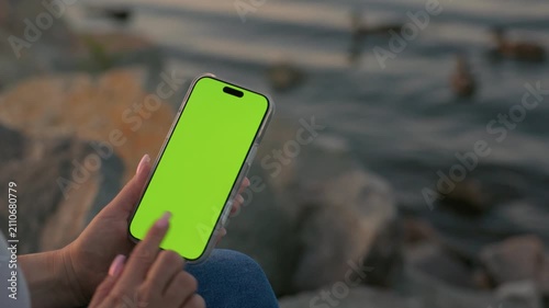 Woman Using Smartphone with Vertical Green Screen Chroma Key Against of River on City Waterfront