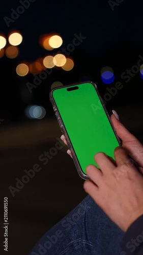 Smartphone with Vertical Green Screen Chroma Key in Woman's Hands Against of Evening City Lights. Vertical Video