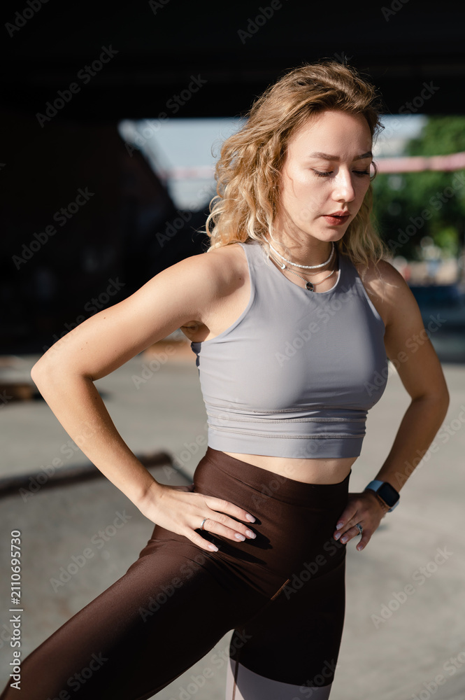 Fototapeta premium Young woman in athletic wear posing outdoors with hands on hips