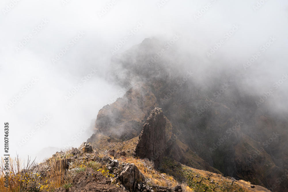 Fototapeta premium A rocky ridge peak wrapped in swirling mist on the PR1 trail, Madeira