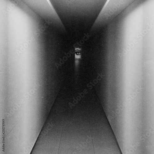 Abstract collage illustration of human eye watching from darkness at end of a long, dimly lit, sinister corridor. Grunge, motion, noise and blur effect applied