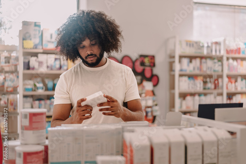 Young man with afro hair reading medication information on box in pharmacy