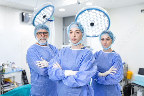 Medical team in operating room. Professional surgeons standing with crossed arms, Hospital and surgery concept. Doctors wearing blue scrubs and surgical caps ready for operation.