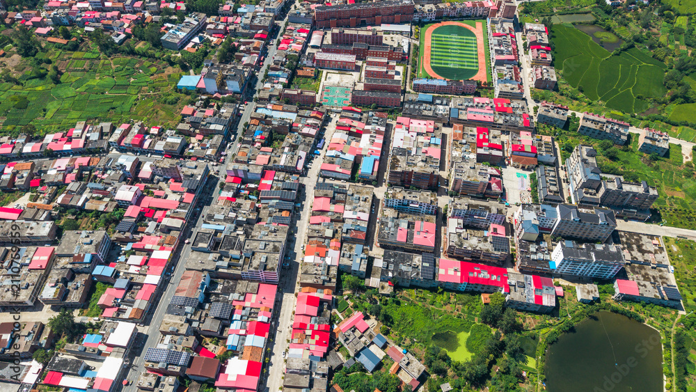 Fototapeta premium Aerial view of densely packed rural houses with a school playground and surrounding farmland