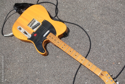 Canvas Print Yellow butterscotch Telecaster style electric guitar lying on asphalt pavement with pick and guitar cable