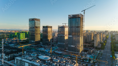 Schilderij op canvas Urban high-rise construction site with cranes and glass facades bathed in mornin