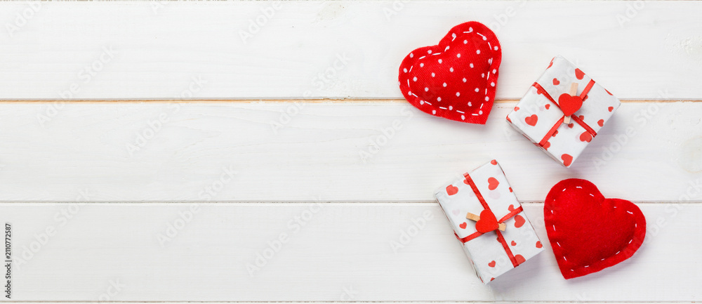 Fototapeta premium Valentine or other holiday handmade present in paper with red hearts and gifts box in holiday wrapper. Present box gift on white wooden table top view with copy space, empty space for design