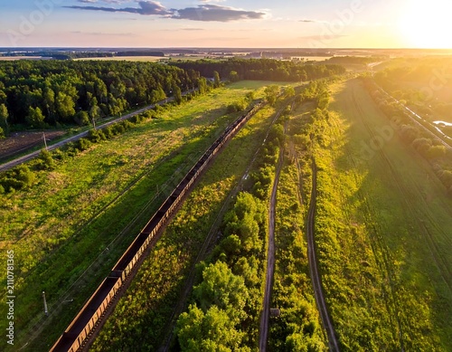 Aerial view captures a train on tracks winding through a vibrant green landscape at sunset, with golden light