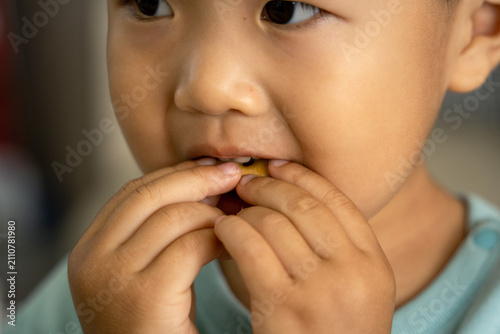 A close-up of a young Asian boy eating a cookie.