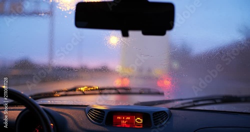 Car driving behind truck on highway in heavy rain at sunset with windshield wipers and colorful twilight bokeh lights