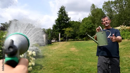 Hosepipe ban. A man points to a watering can as a person uses a hose pipe during a hosepipe ban. Summer drought and water rationing. Water restrictions. 
