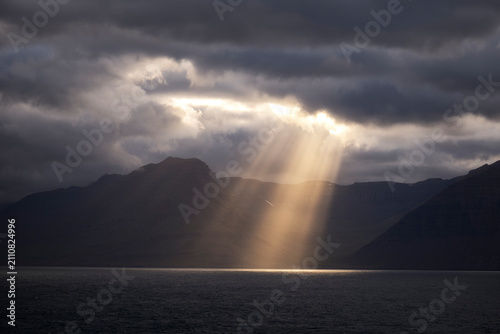 A bright sunbeam pierces a dark cloud over the ocean in Iceland