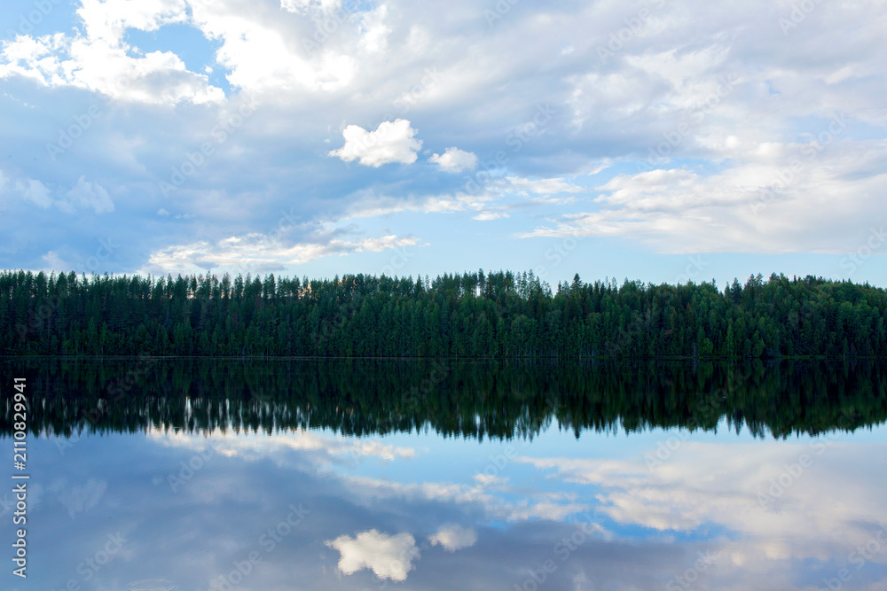 Fototapeta premium Beautiful sunny landscape by the lake in Finland. Clear water with blue and cloudy sky.