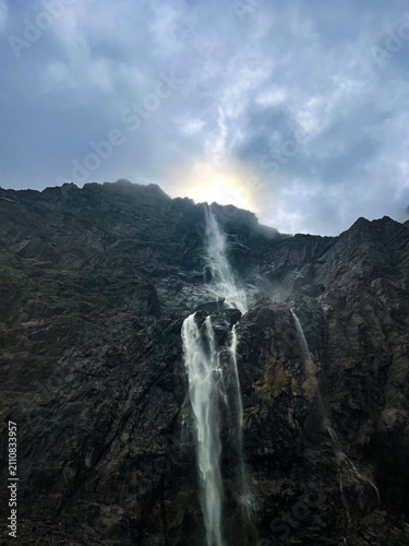 Garvarnie Falls in French Pyrenees, dramatic waterfall pouring between dark rocky cliffs under cloudy sky